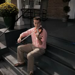 Student playing the violin on the steps of a campus building