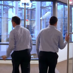 Still from video showing 2 identical employees walking through door
