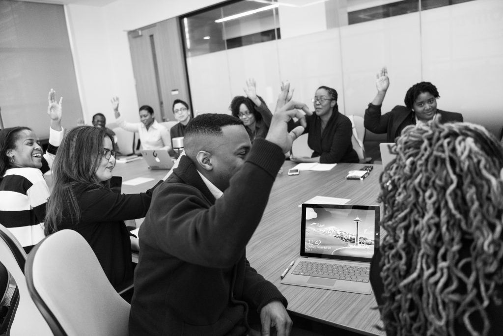 A diverse group of employees raise their hand at a conference table